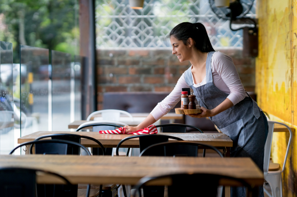 Professionele schoonmaker poetst houten tafels in restaurant voor hygiënische eetruimte
