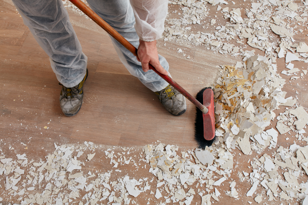 Man veegt bouwstof en brokstukken van vloer tijdens professionele schoonmaak na renovatie