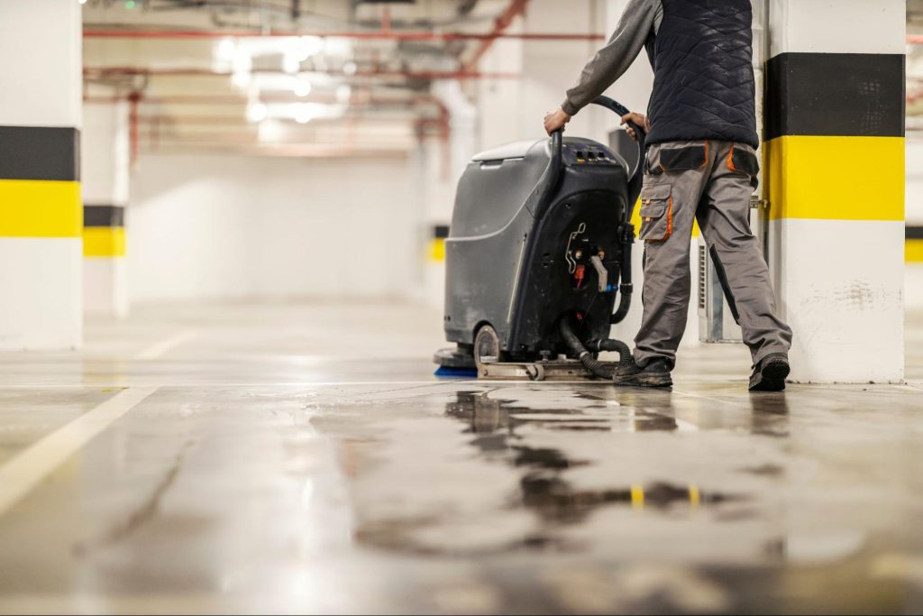 Medewerker reinigt vloer van ondergrondse parking met schrobmachine