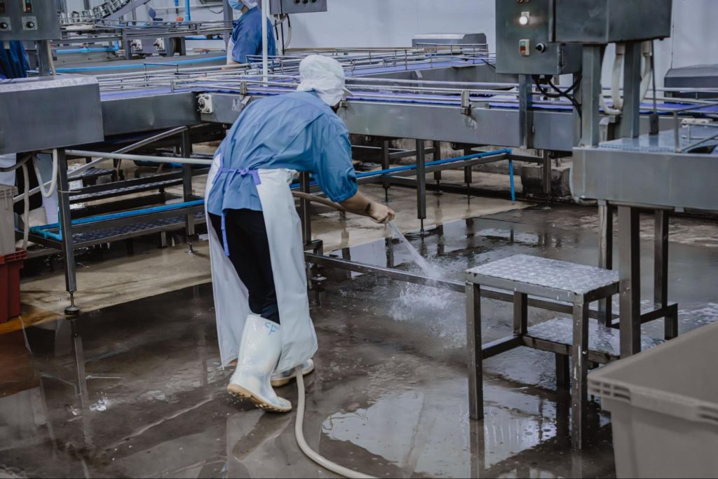 Schoonmaker spuit productievloer schoon in een slachthuis