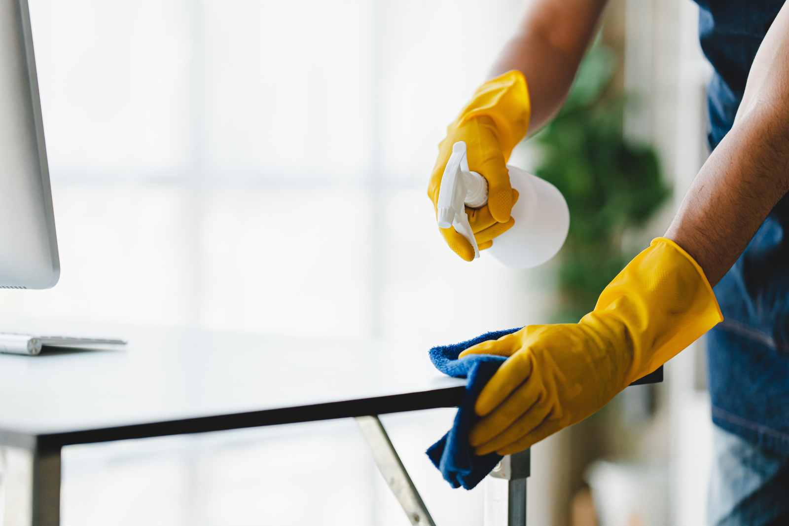 Schoonmaker reinigt een bureau in een klaslokaal met spray en microvezeldoek