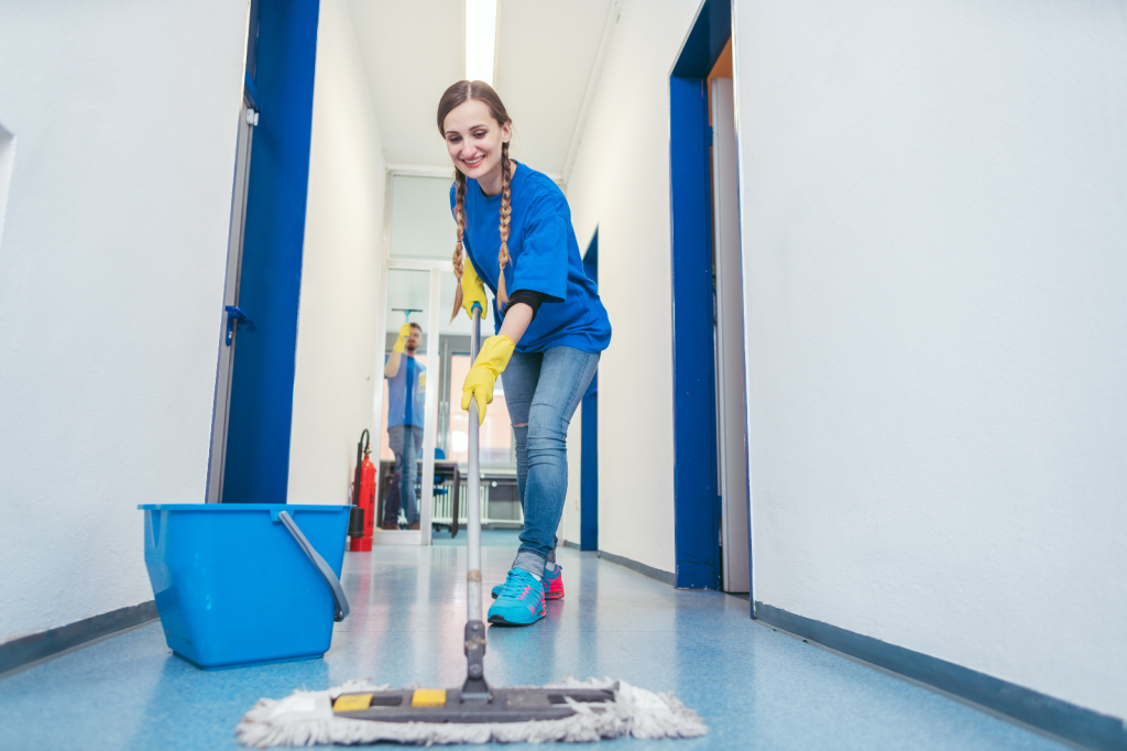 Medewerker van schoonmaakbedrijf reinigt lachend de vloer van een kantoorgang